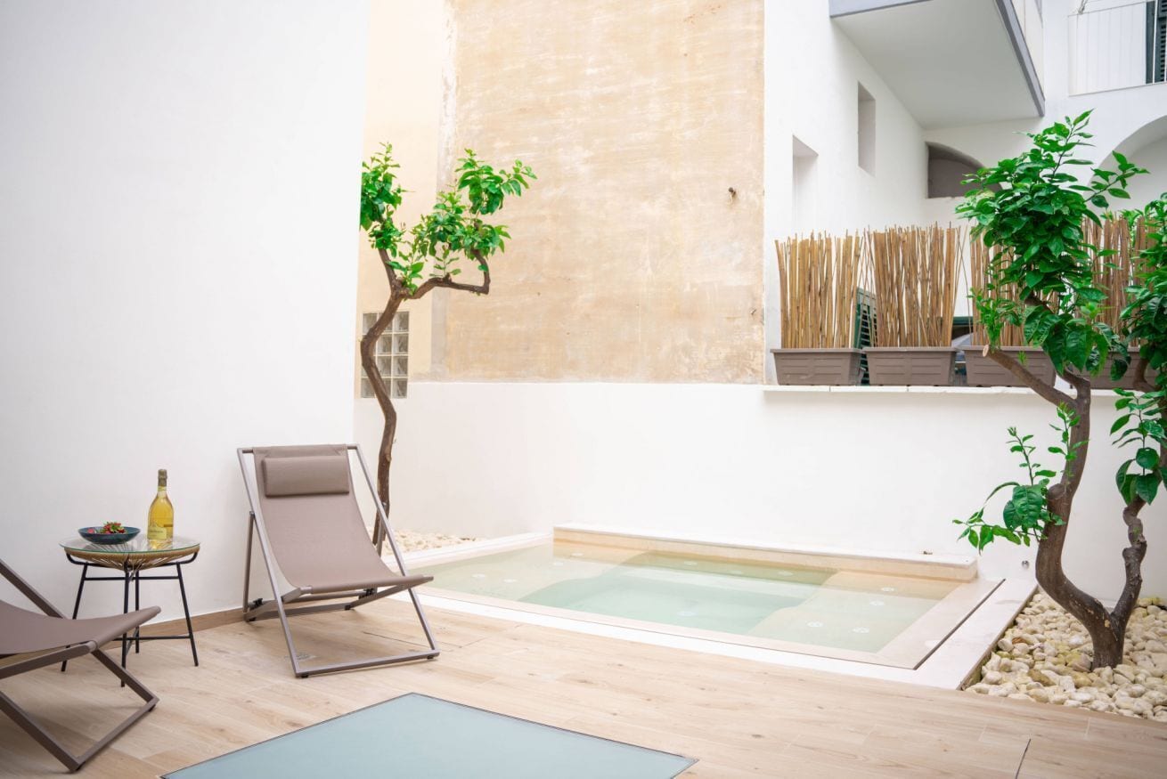 A modern outdoor space with a pool, lounge chairs, and a small table with a bottle.