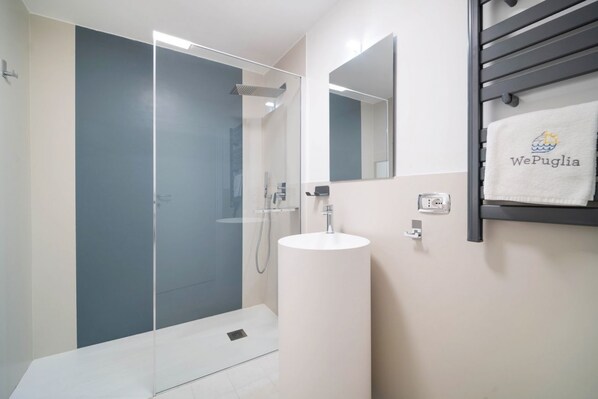 Une salle de bain moderne avec une douche à parois de verre, un lavabo blanc et un porte-serviettes orné d’une serviette de marque.