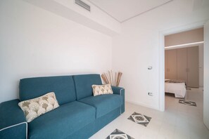 Un salon moderne avec un canapé bleu, des coussins à motifs et un couloir menant à une chambre.