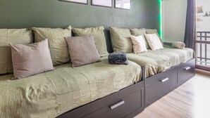 A long, dark-colored sofa with multiple cushions, a blanket, and a folded item. There are three framed pictures on the wall above the sofa. - Beautiful renovated studio, balcony, 4pers (Chamrousse)