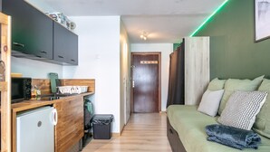 A compact room with a kitchenette, a bed with pillows, and a wooden floor. - Beautiful renovated studio, balcony, 4pers (Chamrousse)
