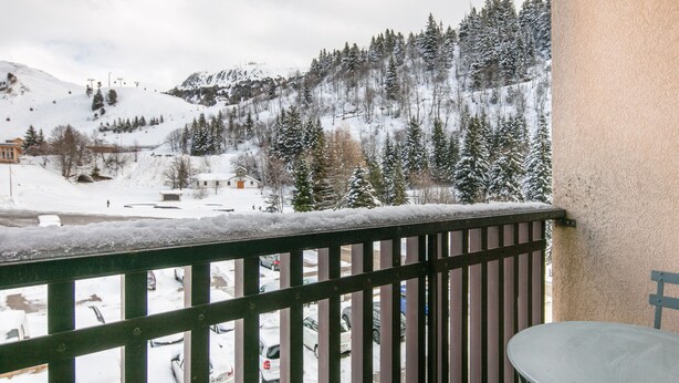 A balcony with a view of a snowy mountain, a parking area with cars, and a table. - Beautiful renovated studio, balcony, 4pers (Chamrousse)