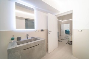 Une salle de bain moderne avec un grand miroir, un lavabo et une porte donnant sur une autre pièce.