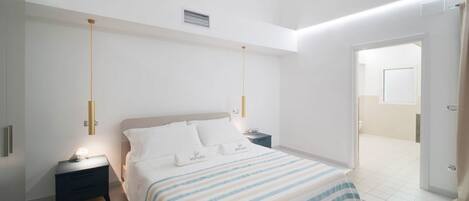 Un dormitorio moderno con una cama, mesitas de noche y una puerta que da a otra habitación.