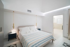 Une chambre à coucher moderne, avec un lit, des tables de chevet et une porte donnant sur une autre pièce.