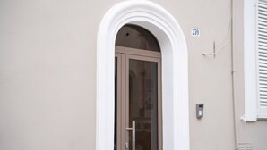 A building entrance with a glass door, a white arched frame, and a number '259' on the wall. - WePuglia - The White Luxury – Apt Ataraxia (Monopoli)