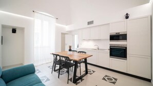 A modern kitchen with white cabinets, a wooden dining table, and black chairs. - WePuglia - The White Luxury – Apt Ataraxia (Monopoli)