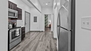 A modern kitchen with stainless steel appliances, a wooden floor, and a view into the living area.