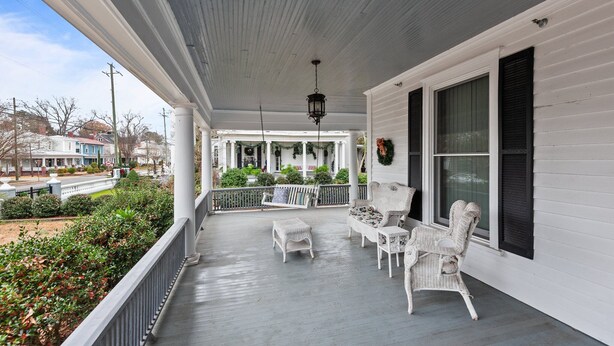 A covered porch with white wicker furniture, a hanging lantern, and a view of the neighborhood.