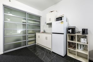 A modern kitchen with a sliding glass door, white cabinets, a microwave, a coffee maker, and a toaster. - 15th Floor Superior Hotel Suite King Bed (Darwin City)
