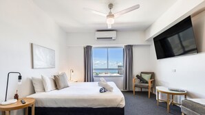 A hotel room with a bed, a chair, a small table, a TV, and a window with a view. - 15th Floor Superior Hotel Suite King Bed (Darwin City)