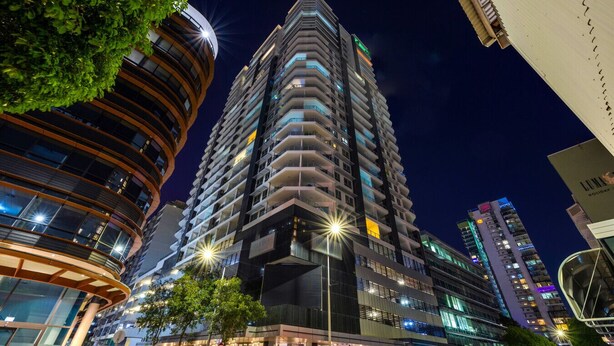 A high-rise hotel with multiple balconies, a curved facade, and illuminated signage. - 15th Floor Superior Hotel Suite King Bed (Darwin City)