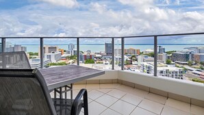Varanda com mesa e cadeiras, com vista para a paisagem urbana e o mar.