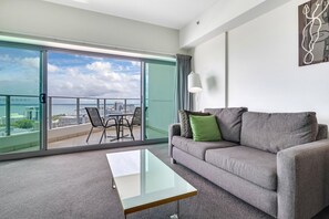 A modern living room with a grey sofa, a glass coffee table, and a view of the city through large sliding glass doors. - Living the Dream on Level 18! (Darwin City)