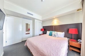 Une chambre d’hôtel avec un grand lit, une télévision, une table de chevet avec une lampe et un miroir.