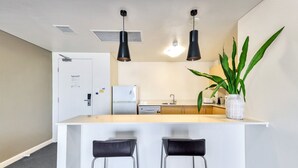 A compact kitchen with a white countertop, two black pendant lights, a refrigerator, a sink, and a potted plant. - Resort Style City View w/ King Bed, Pool, Balcony (Darwin City)