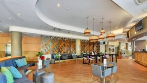 A spacious lobby with a curved ceiling, a seating area with sofas and chairs, a bar area, and a large wall mural. - Resort Style City View w/ King Bed, Pool, Balcony (Darwin City)