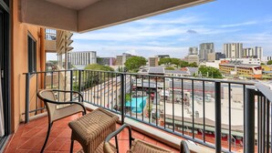 A balcony with wicker furniture, a view of a cityscape with buildings and a parking lot. - Resort Style City View w/ King Bed, Pool, Balcony (Darwin City)