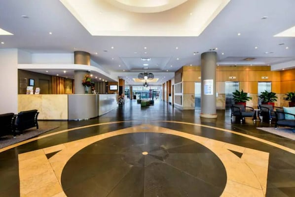 Un hall d’entrée spacieux, doté d’un aménagement circulaire central, d’un comptoir d’accueil, d’un espace salon et d’un plafond moderne avec des luminaires encastrés.