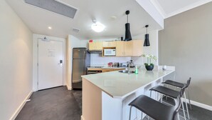 A modern kitchen with a central island, bar stools, and a microwave. - Resort Style Escape w/ King Bed, Pool, Balcony (Darwin City)