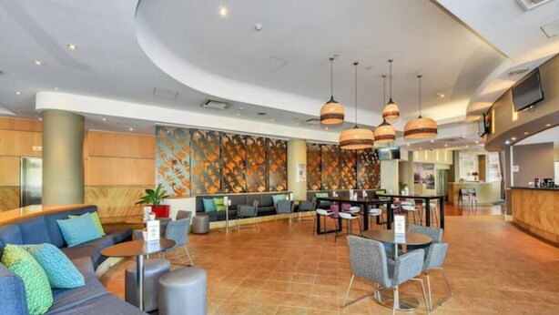 A spacious lobby with a curved ceiling, a seating area with sofas and chairs, a bar area, and a large wall mural. - Resort Style Escape w/ King Bed, Pool, Balcony (Darwin City)