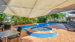 An outdoor swimming pool area with a hot tub, lounge chairs, and tables under a shaded canopy. - Resort Style Escape w/ King Bed, Pool, Balcony (Darwin City)