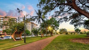 A park with a paved walkway, trees, and a building in the background. - Resort Style Escape w/ King Bed, Pool, Balcony (Darwin City)
