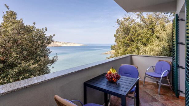 A balcony with a table and chairs, a bowl of fruit, and a view of the sea and hills. - Nice apartment in Lopar with house sea view (Lopar)