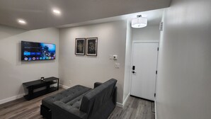 Een moderne woonkamer met een flatscreen televisie, een grijze bank en een klein entertainment meubel.