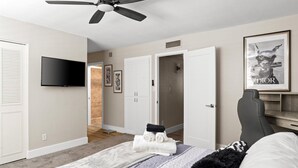 Een slaapkamer met een bed, een plafondventilator, een flatscreen televisie, een ingelijst poster en een deur naar een andere kamer.