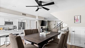 Een moderne keuken met witte kastjes, roestvrijstalen apparatuur en een donker houten eettafel met zes stoelen.