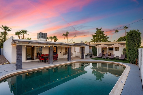 Relax in a serene outdoor space with a pool, patio seating, and lush greenery.