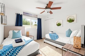 Two beds with matching headboards and ceiling fan, surrounded by artwork and decorative accents.