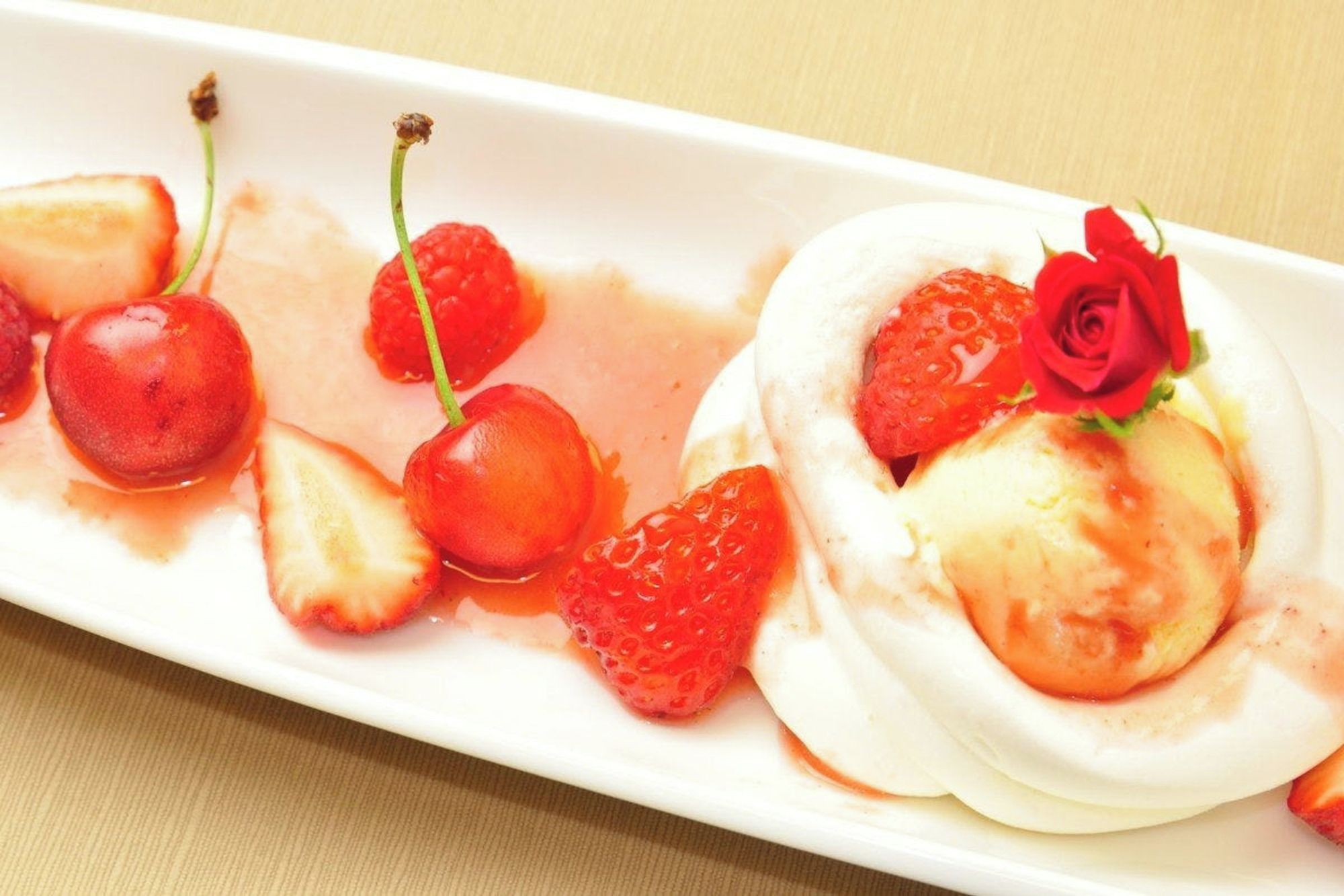 A dessert plate with a meringue, strawberries, cherries, and a rose decoration.