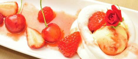 A dessert plate with a meringue, strawberries, cherries, and a rose decoration.