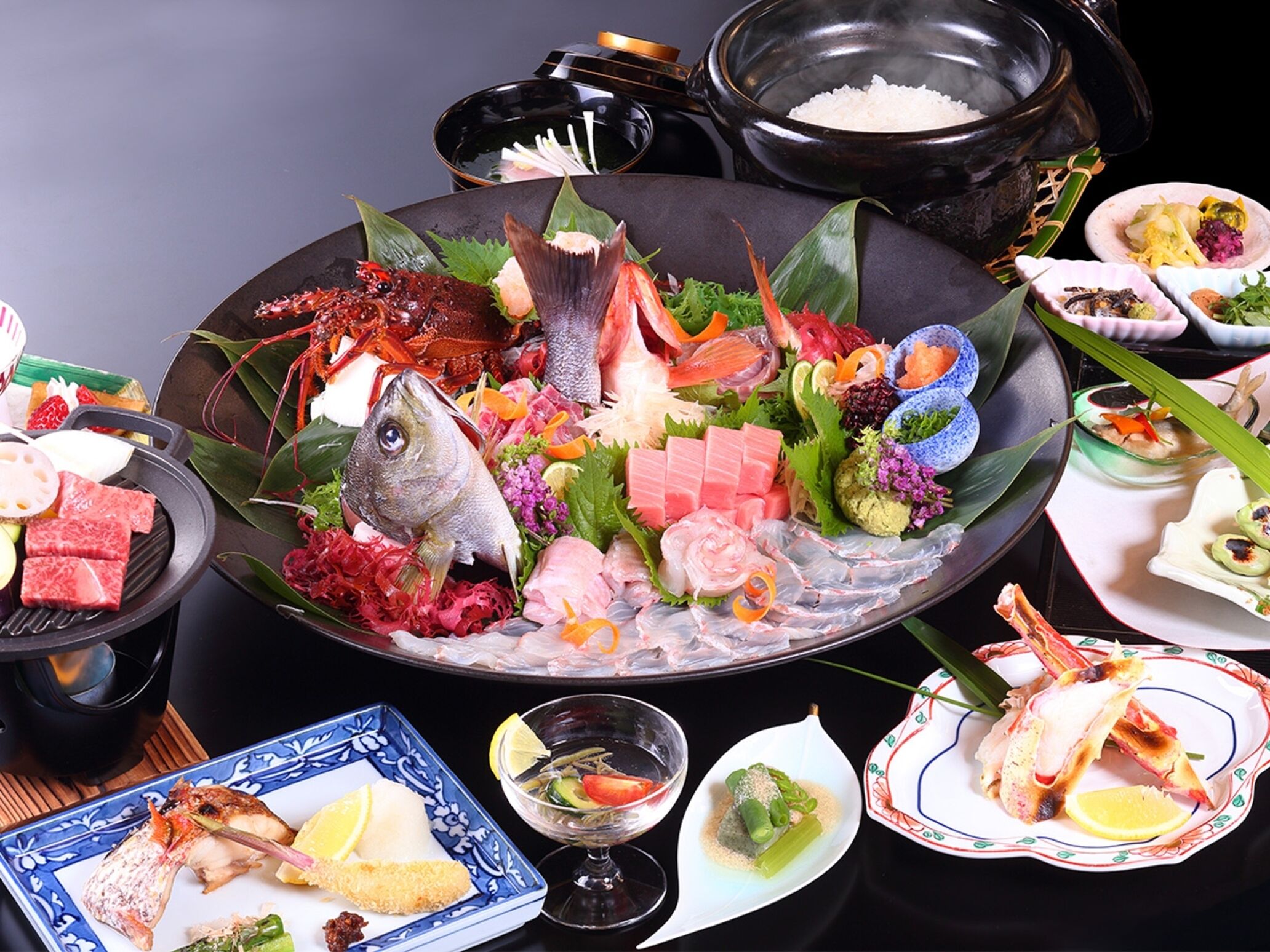 A variety of seafood dishes on a large platter, including fish, shrimp, and other seafood items, with a pot of rice and small bowls of condiments.