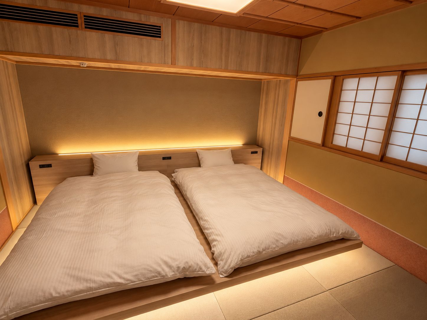 A traditional Japanese-style room with tatami flooring, a low wooden headboard, and sliding shoji doors.