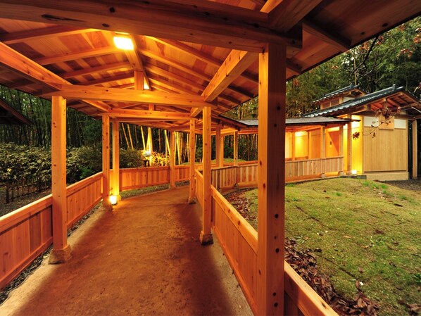 Une allée couverte en bois mène à un bâtiment traditionnel doté d’un toit en tuiles.