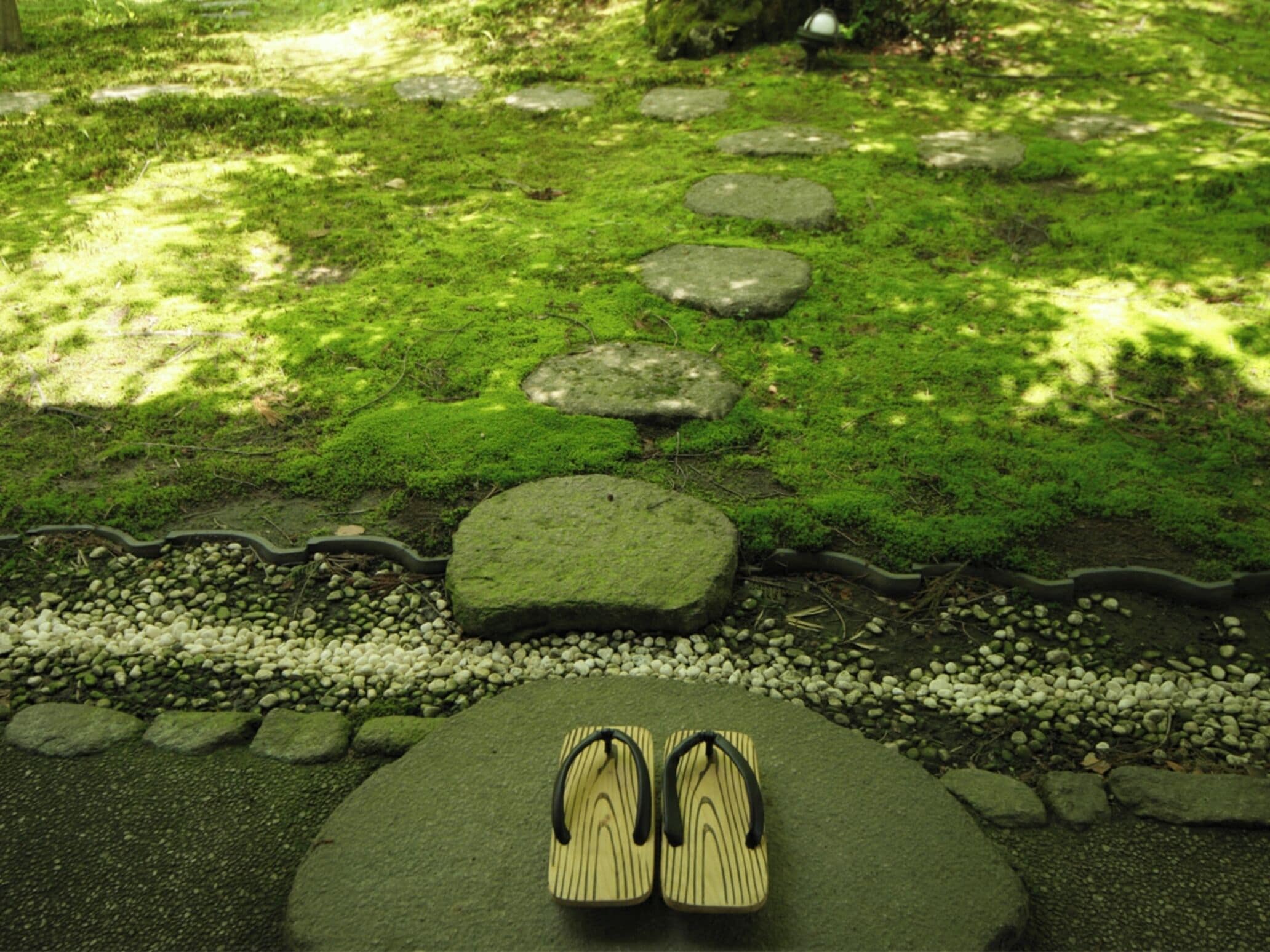 A pair of flip-flops on a moss-covered stone path in a garden.