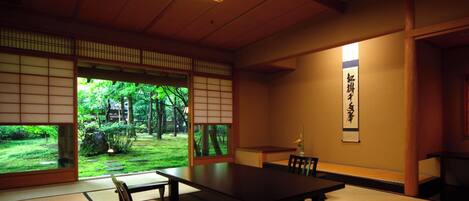 Una habitación japonesa tradicional con suelo de tatami, una mesa baja y vistas a un jardín exuberante.