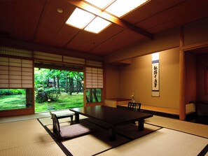 Ett traditionellt japanskt rum med tatamimattor på golvet, ett lågt bord och utsikt över en frodig trädgård.