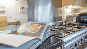 Een keuken met een fornuis, een magnetron en een boek op het aanrecht.