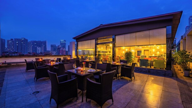 An outdoor dining area with tables and chairs, a city skyline in the background, and a building with large windows. - HOWDY SMART HOTEL (Chengdu)