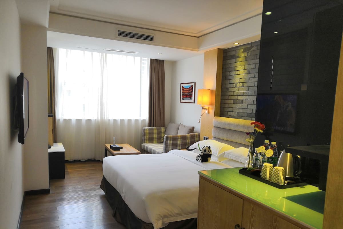 A hotel room with a bed, a sofa, a desk, a TV, and a window with curtains.
