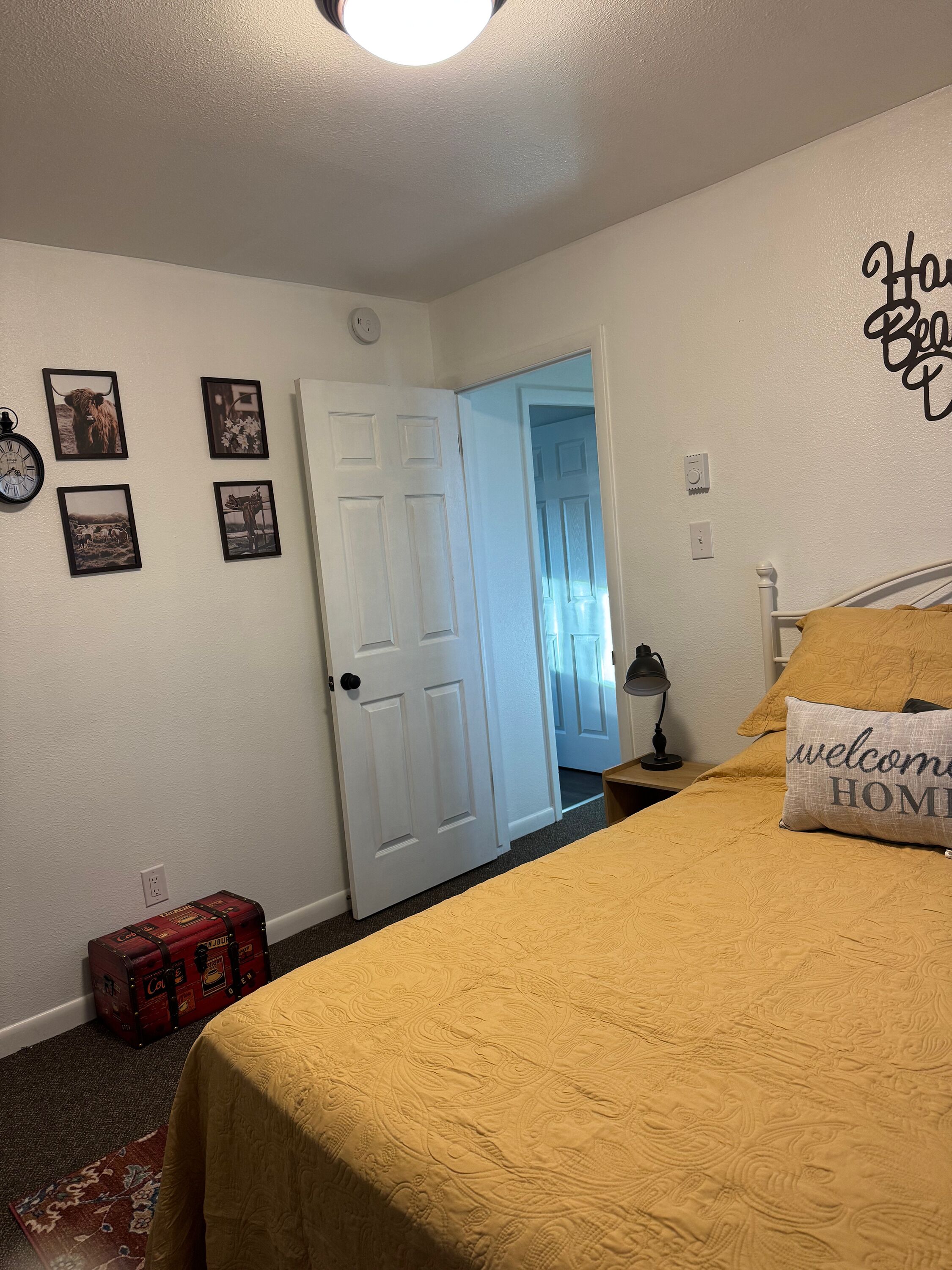 Un dormitorio con cama, una puerta, un reloj de pared y cuadros enmarcados.