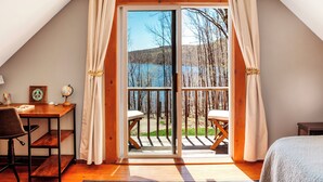 A bedroom with a large sliding glass door leading to a balcony with a view of a lake and trees.