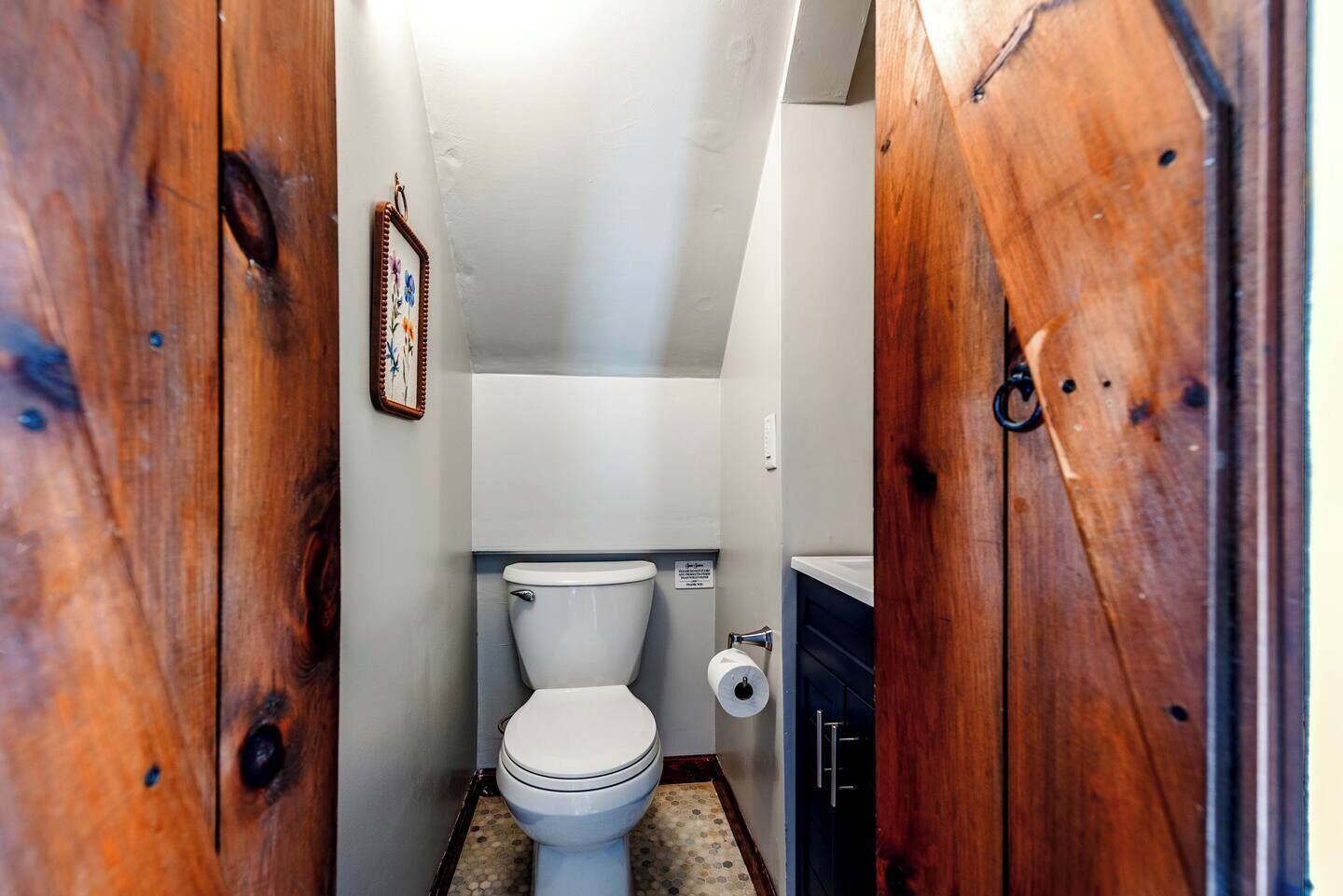 A small, narrow bathroom with a toilet, a roll of toilet paper, and a wooden cabinet.