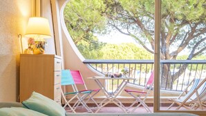 Ein Balkon mit Tisch für zwei Personen, einem Bett mit Kissen und Blick auf Bäume und ein Gebäude.