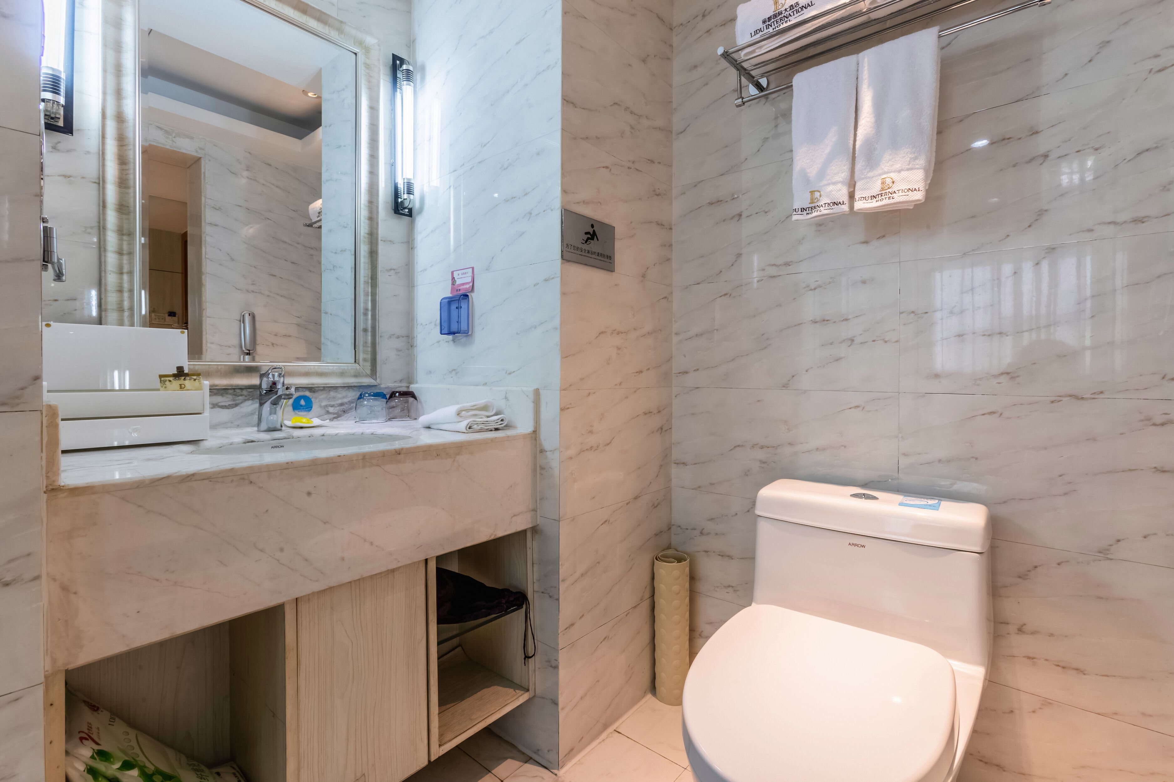 Ein modernes Badezimmer mit einem мраморным Waschbecken, einem großen Spiegel, einer Toilette und einem Handtuchhalter.