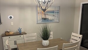 A dining area with a wooden table, white chairs, a potted plant, and a pendant light. - Surfside Hideaway! Dog friendly 3 bed, 2 bath home. Only 1 mile to beach! (Myrtle Beach)